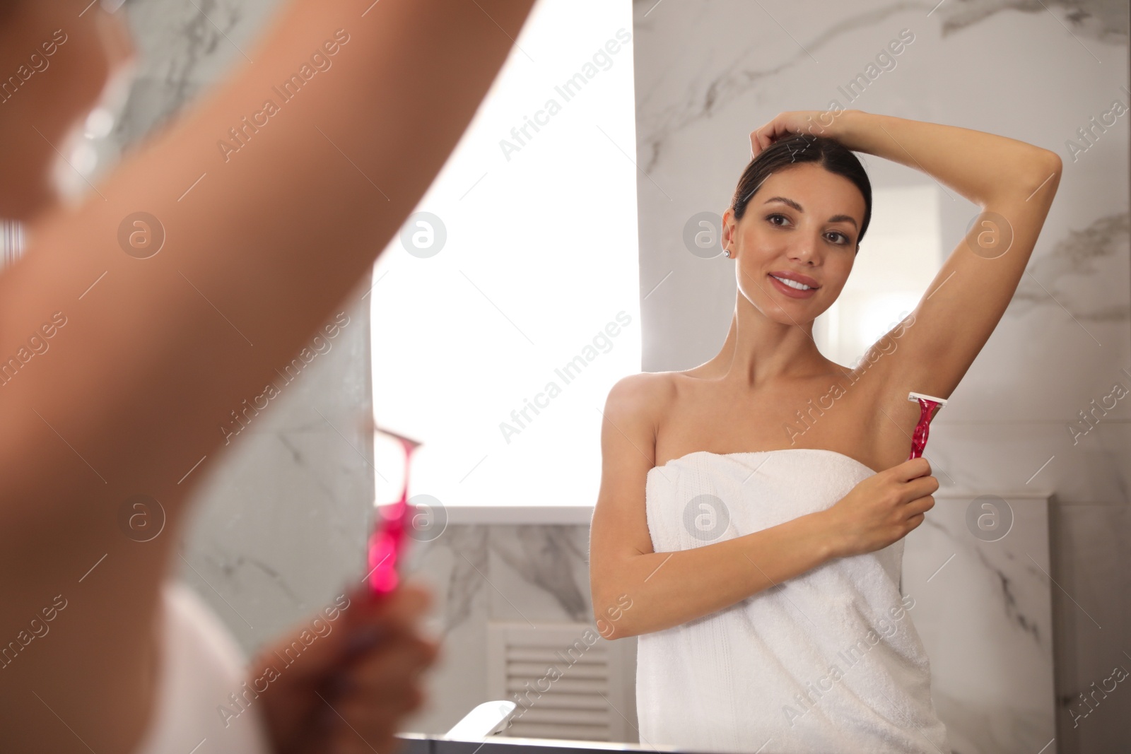 Photo of Young woman shaving her armpit in bathroom