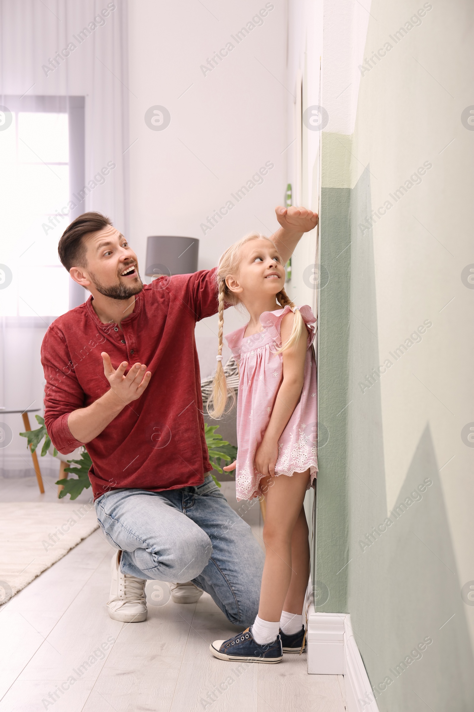 Photo of Young man measuring his daughter's height at home