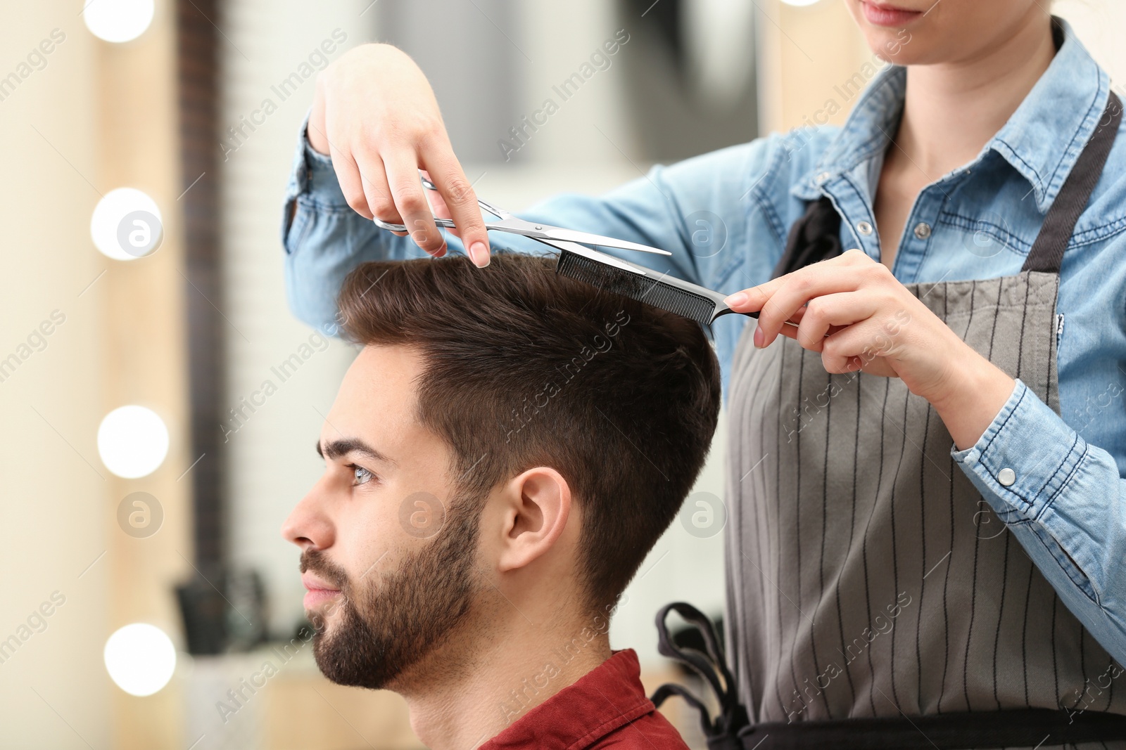 Photo of Barber making stylish haircut with professional scissors in beauty salon