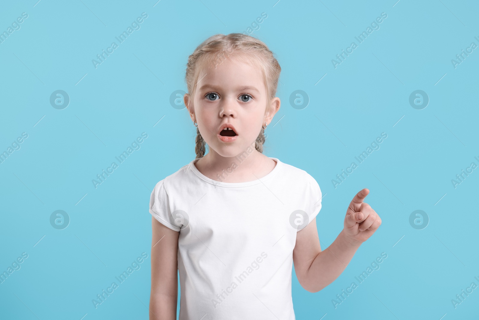 Photo of Cute little girl pointing at something on light blue background