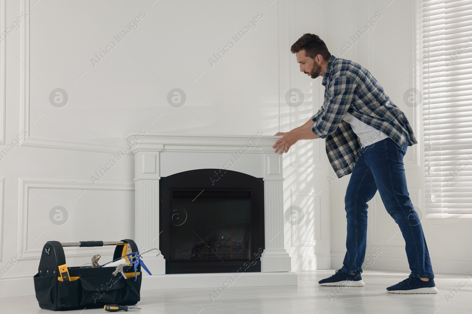 Photo of Man installing electric fireplace near white wall in room