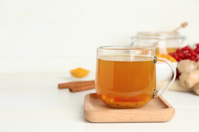 Photo of Glass cup of immunity boosting tea with ingredients on white wooden table. Space for text