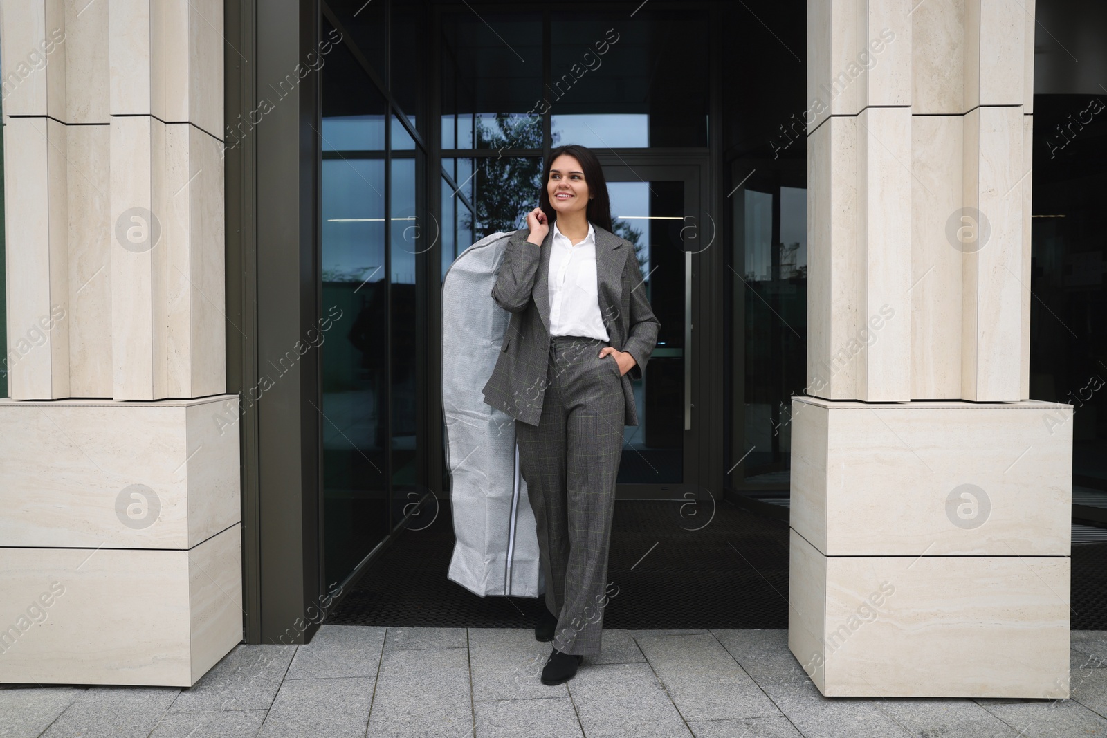 Photo of Attractive happy businesswoman holding garment cover with clothes outdoors. Dry cleaning service