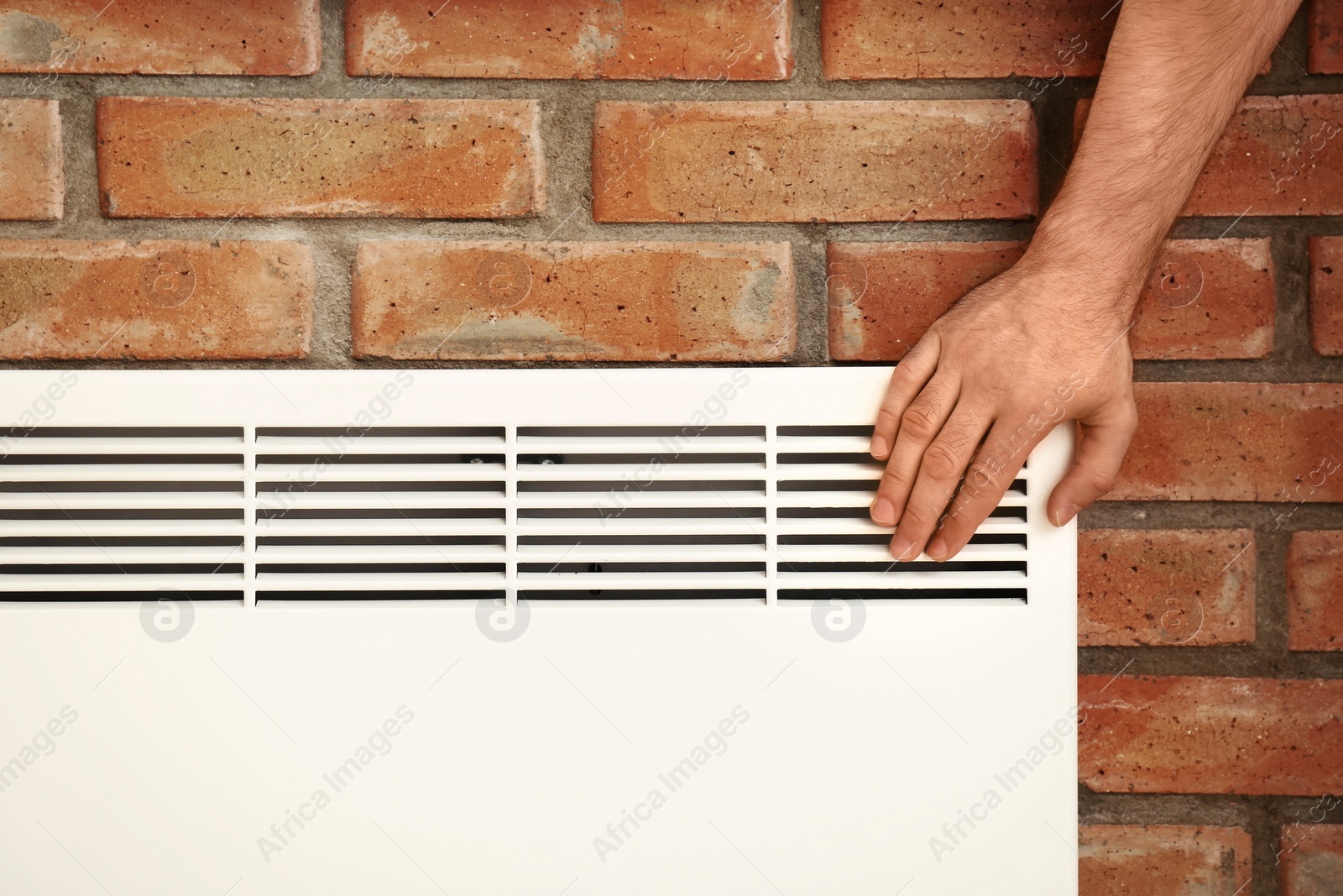 Photo of Man checking temperature of heating convector on brick, closeup