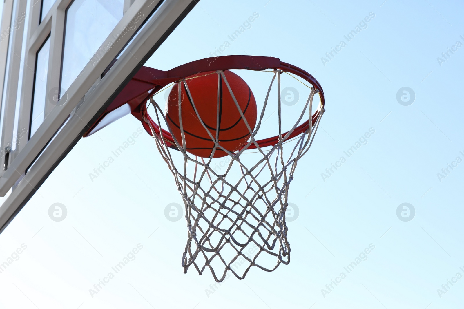 Photo of Basketball ball and hoop with net outdoors on sunny day