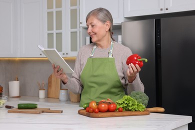 Photo of Happy woman with recipe book and bell pepper in kitchen