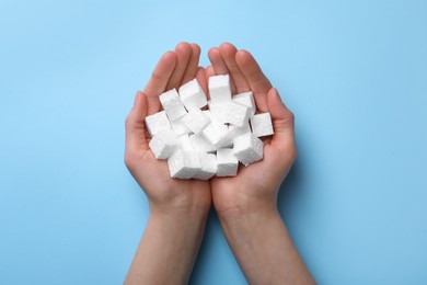 Photo of Woman with handful of styrofoam cubes on light blue background, top view