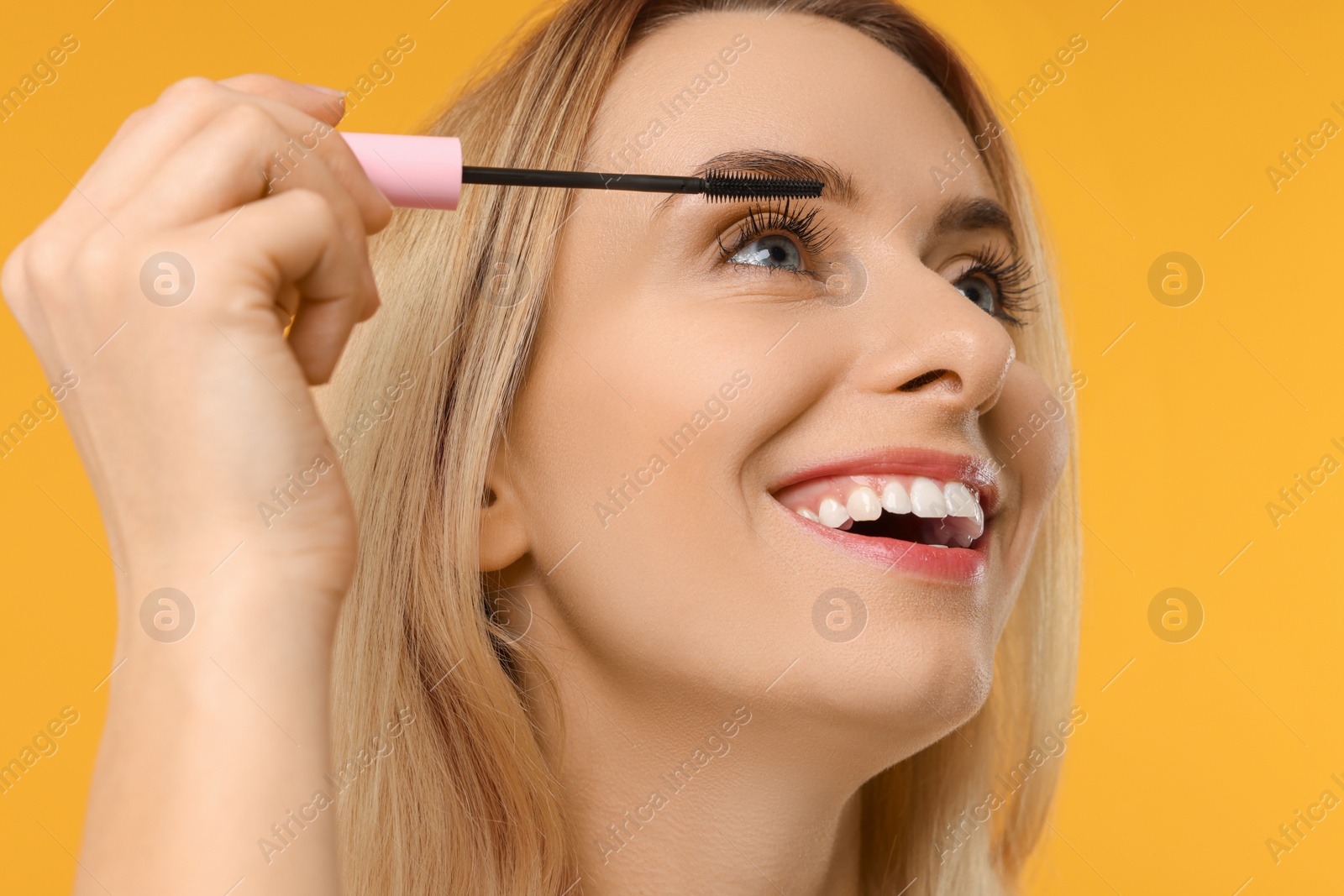 Photo of Beautiful woman applying mascara on orange background, closeup