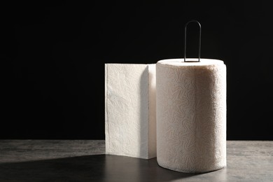 Photo of Holder with roll of white paper towels on grey table against black background. Space for text