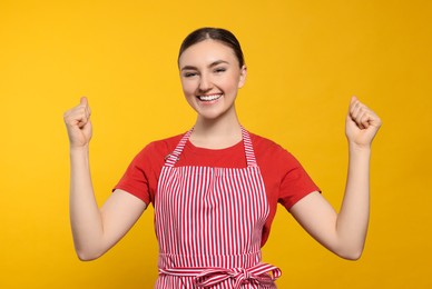 Photo of Beautiful young woman in clean striped apron on orange background