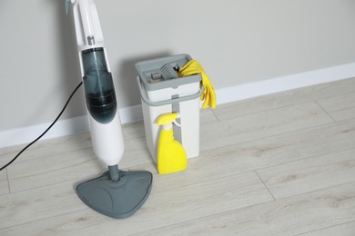 Modern steam mop, bucket with gloves and spray of cleaning product on floor near grey wall. Space for text