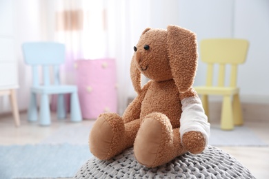 Photo of Toy bunny with bandaged pad on pouf indoors, space for text. Children's doctor