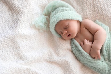 Photo of Cute newborn baby in warm hat sleeping on white plaid, above view. Space for text