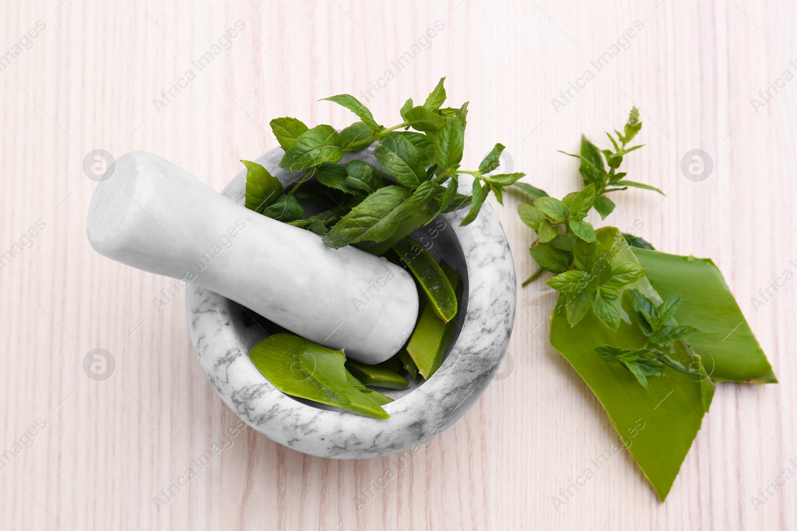 Photo of Mortar with pestle, aloe and mint leaves on wooden table, top view
