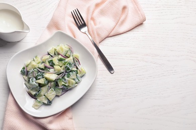 Photo of Flat lay composition with plate of creamy cucumber salad and space for text on wooden table