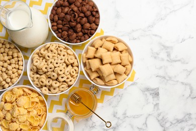 Photo of Different breakfast cereals, honey and milk on white marble table, flat lay. Space for text