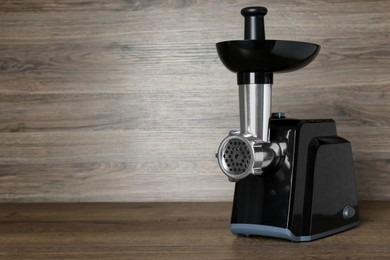 Photo of Modern electric meat grinder on wooden table. Space for text