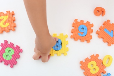 Photo of Little girl playing with colorful puzzles at white table, top view. Educational toy