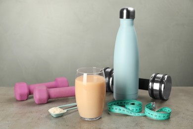 Photo of Tasty shake, bottle, measuring tape, dumbbells and powder on gray table, space for text. Weight loss