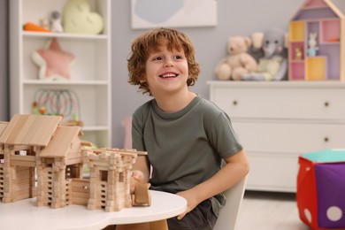 Photo of Little boy playing with wooden entry gate at white table in room. Child's toy