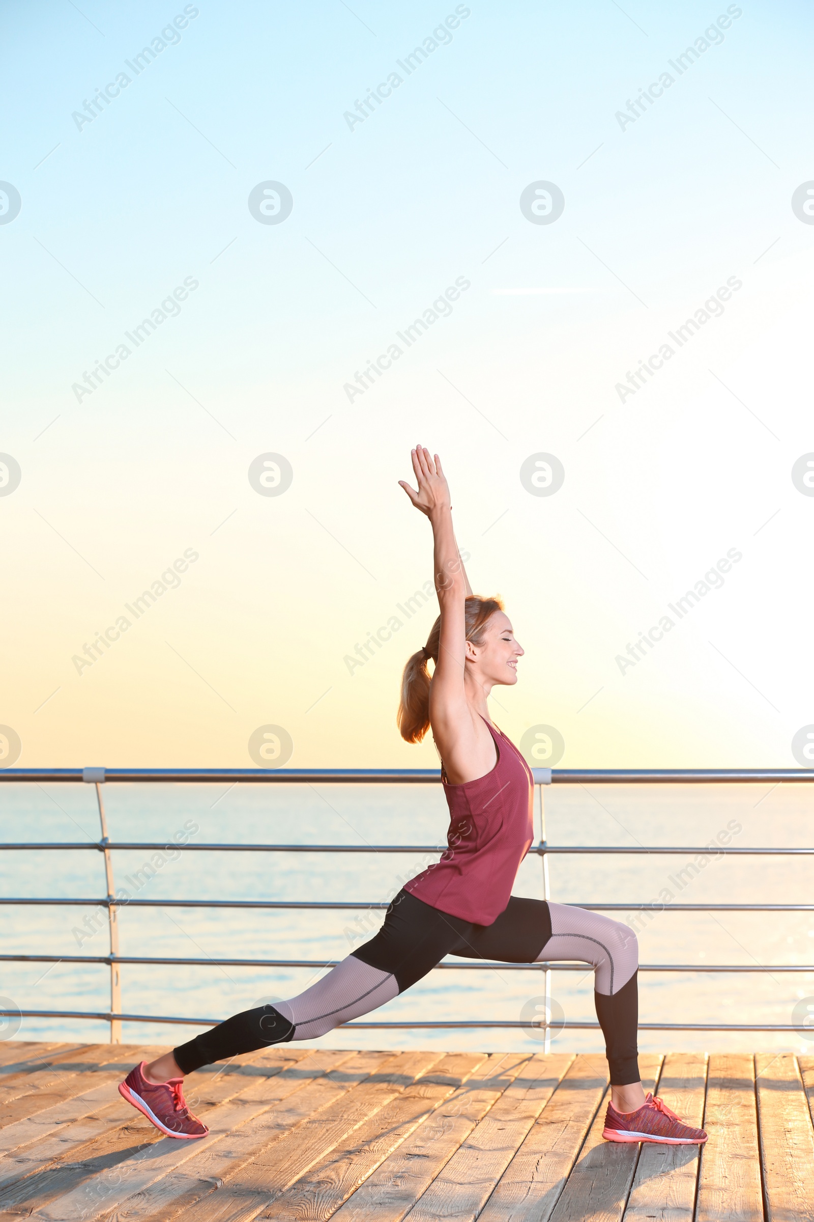 Photo of Young woman doing fitness exercises on pier in morning