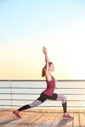 Young woman doing fitness exercises on pier in morning