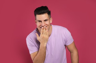 Handsome man laughing on maroon background. Funny joke