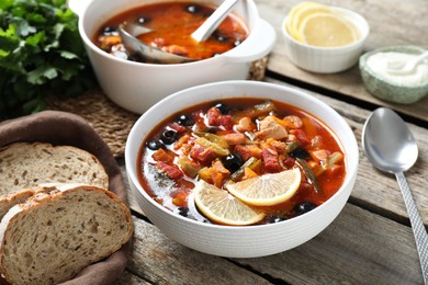Photo of Meat solyanka soup with sausages, olives and vegetables served on wooden table