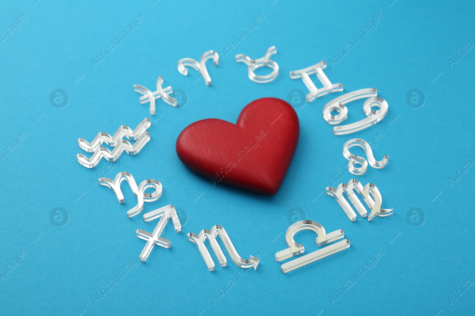 Photo of Zodiac signs and heart on light blue background, closeup