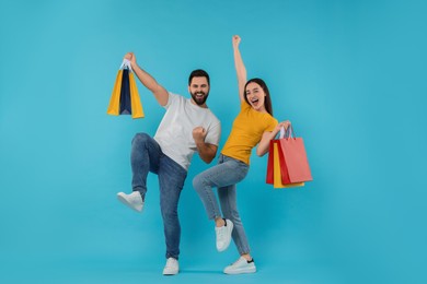 Photo of Happy couple with shopping bags having fun on light blue background