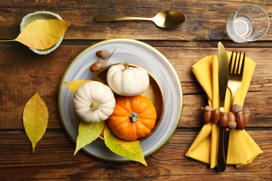 Seasonal table setting with pumpkins and other autumn decor on wooden background, flat lay