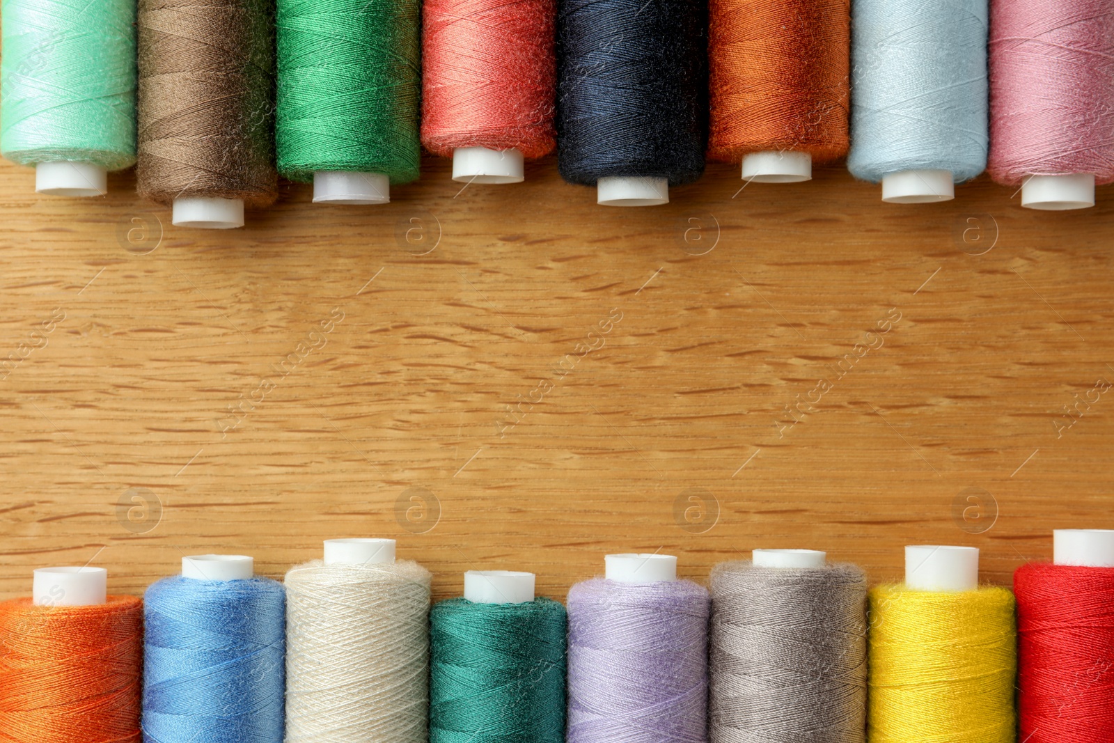 Photo of Many colorful sewing threads on wooden table, flat lay. Space for text