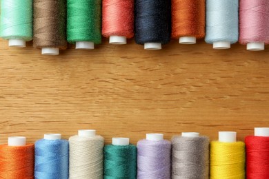 Photo of Many colorful sewing threads on wooden table, flat lay. Space for text