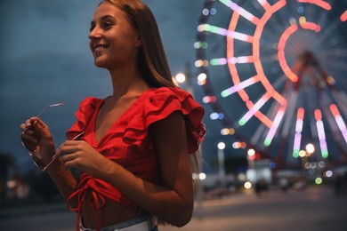 Photo of Beautiful young woman against glowing Ferris wheel in amusement park, space for text