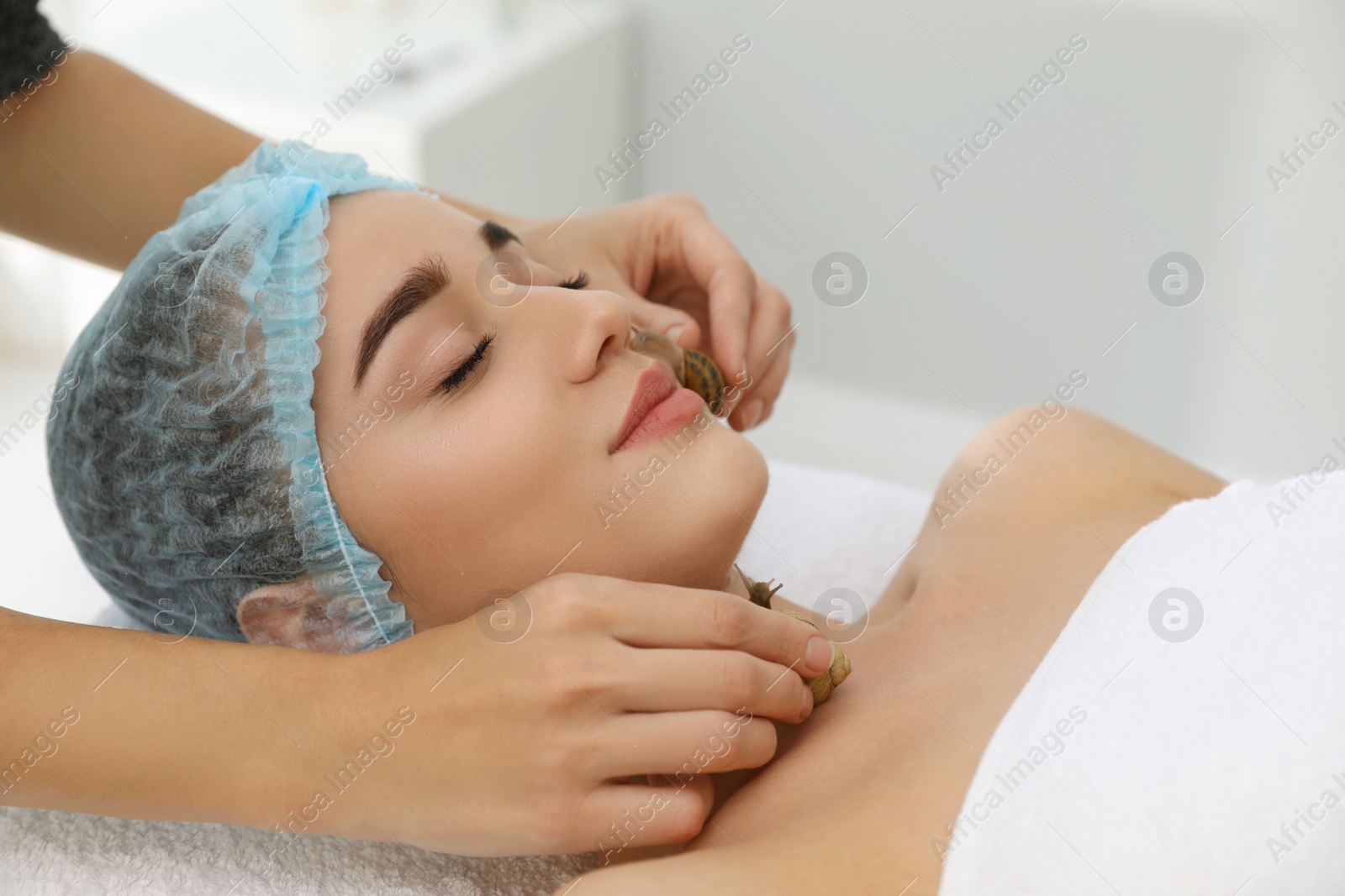 Photo of Young woman receiving snail facial massage in spa salon, closeup