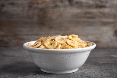 Photo of Bowl with sweet banana slices on grey table, space for text. Dried fruit as healthy snack