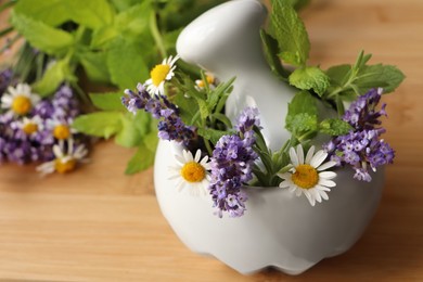 Mortar with fresh lavender, chamomile flowers, herbs and pestle on wooden table, closeup