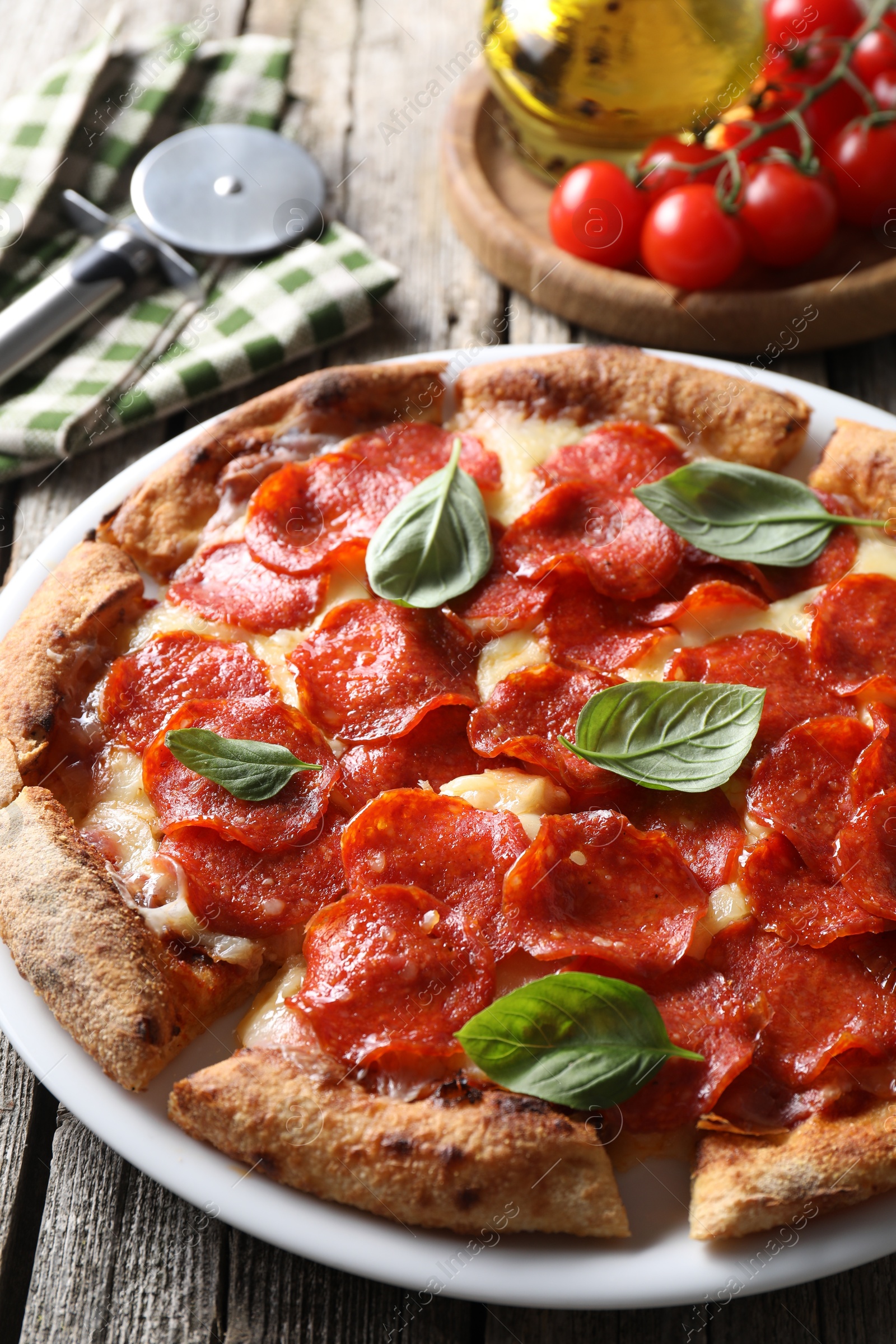 Photo of Tasty pepperoni pizza with basil, tomatoes and cutter on wooden table