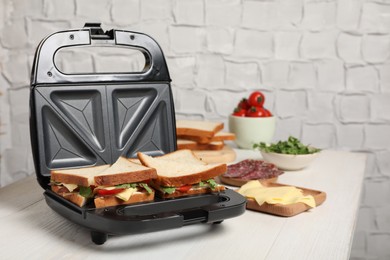 Modern grill maker with tasty sandwiches and ingredients on white wooden table