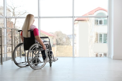 Mature woman sitting in wheelchair near window at home