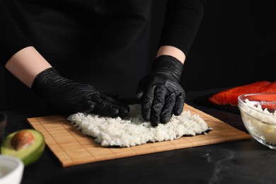 Photo of Chef in gloves making sushi roll at dark table, closeup