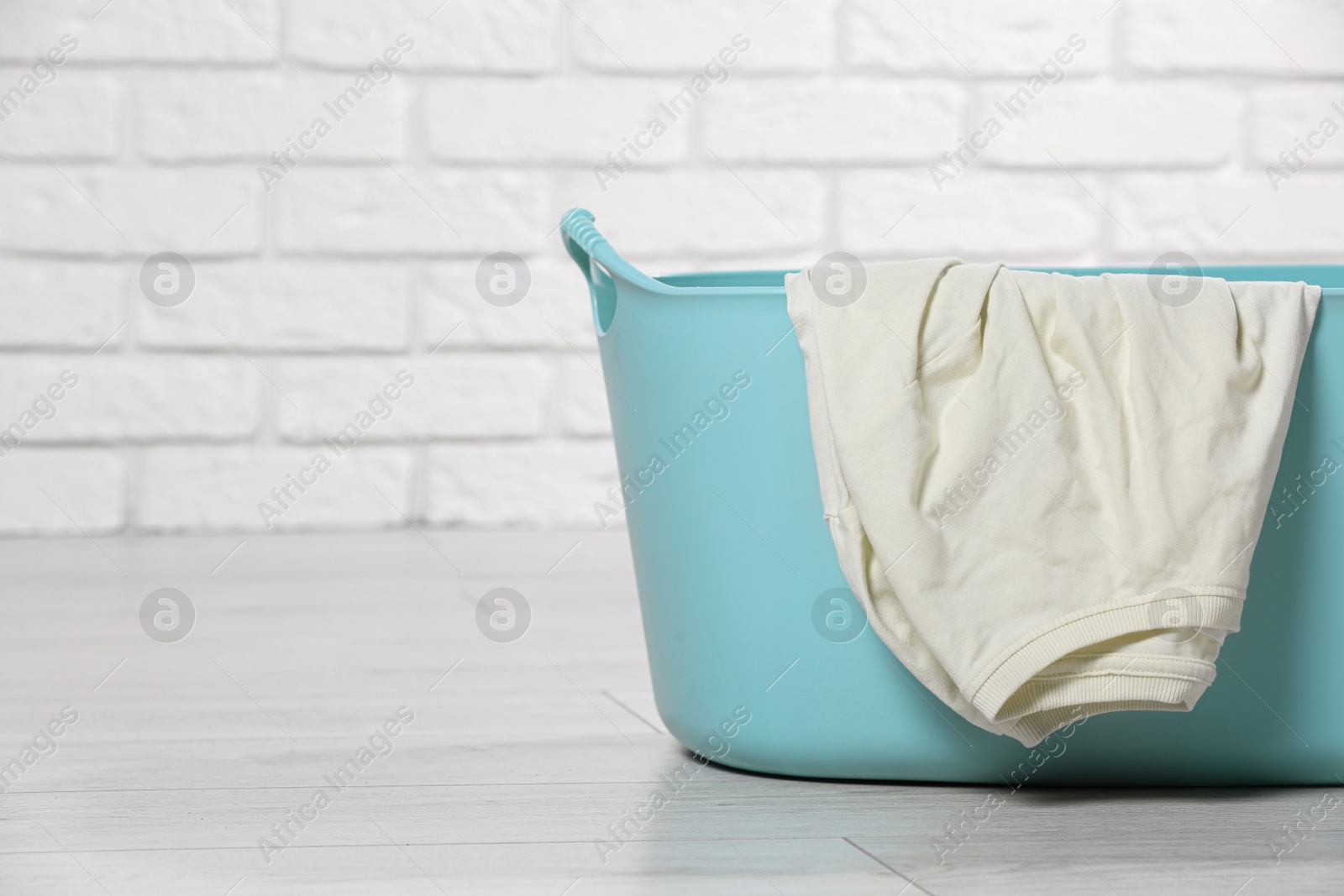 Photo of Laundry basket with clothes near white brick wall. Space for text