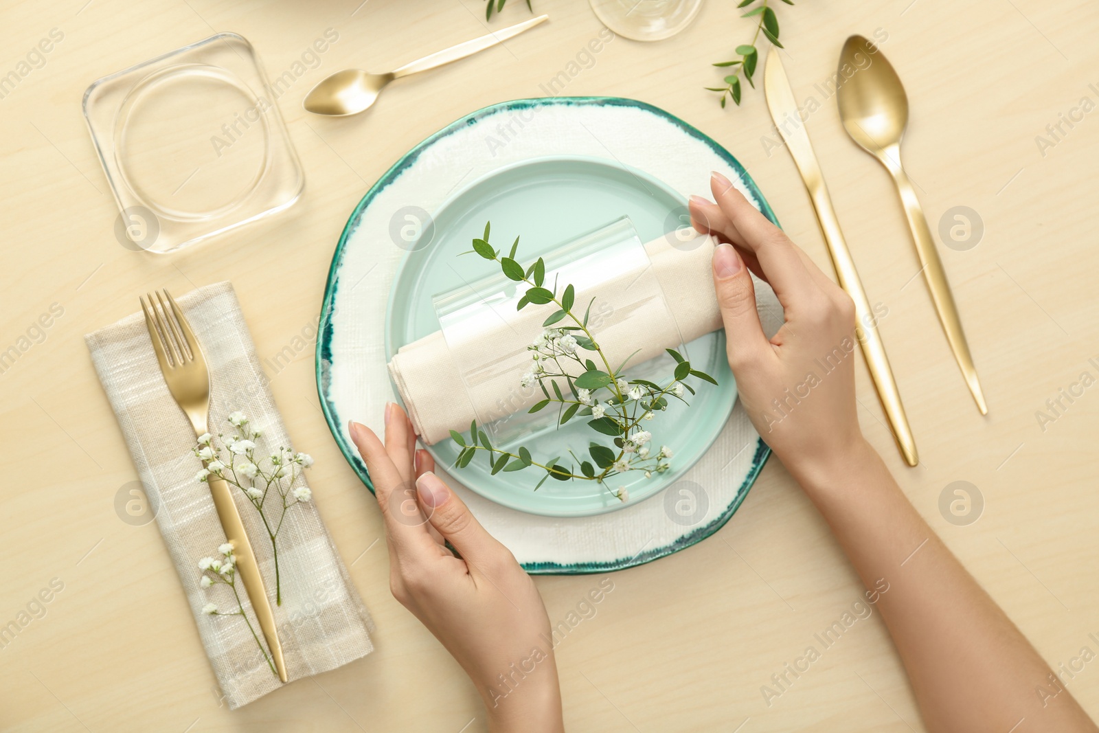 Photo of Woman setting table with green leaves for festive dinner, top view