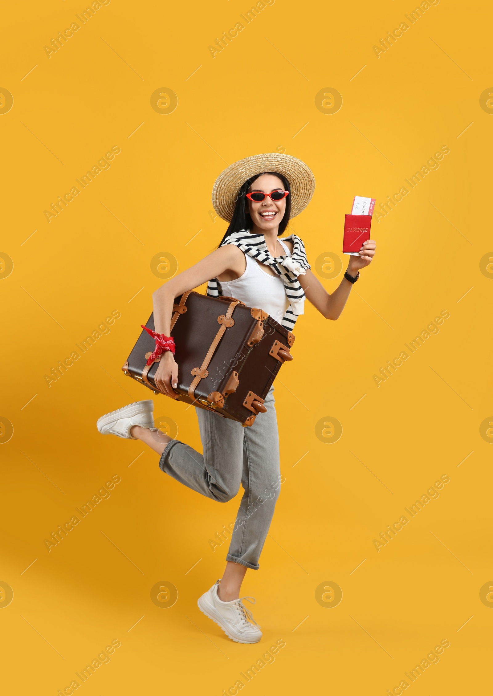 Photo of Happy female tourist with passport, ticket and suitcase on yellow background