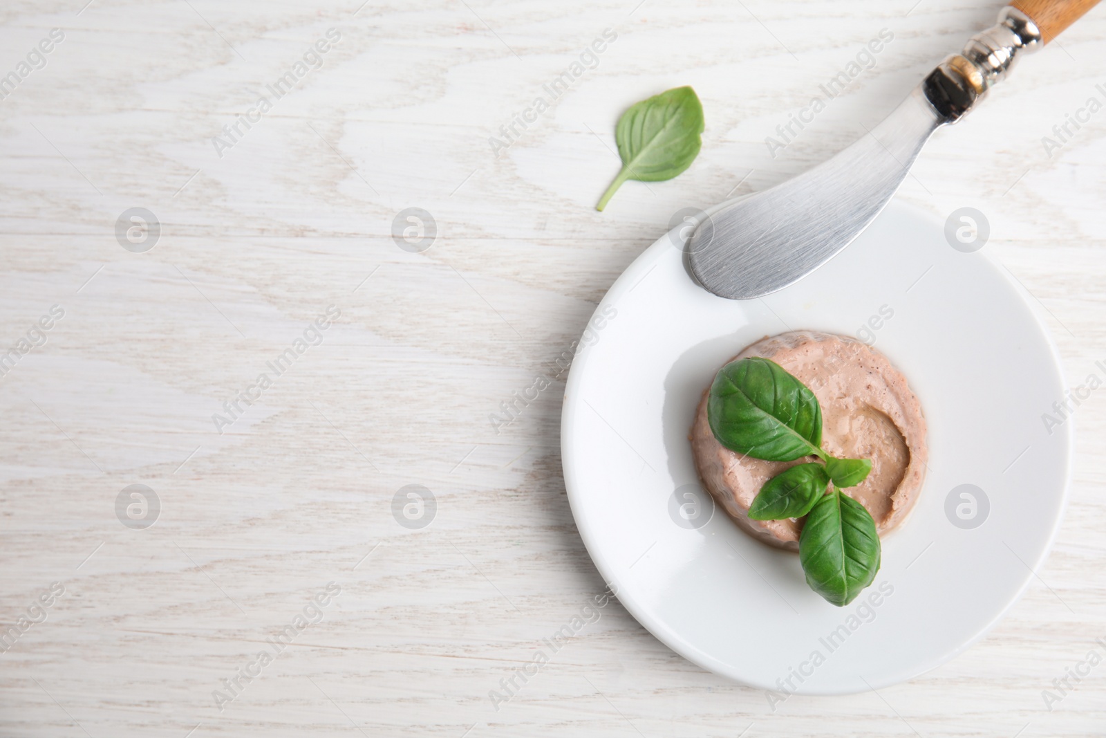 Photo of Plate with delicious meat pate, basil and knife on white wooden table, flat lay. Space for text