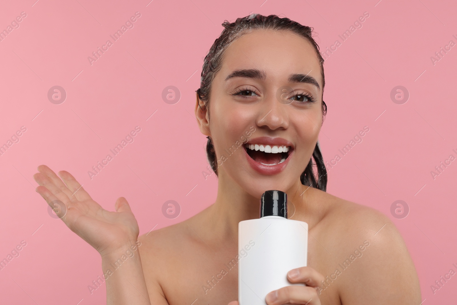Photo of Washing hair. Portrait of beautiful happy woman with bottle singing on pink background