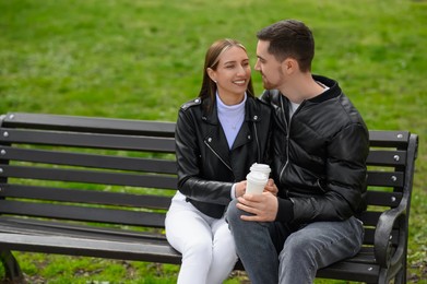 Photo of Lovely young couple with cups of coffee on bench outdoors. Romantic date