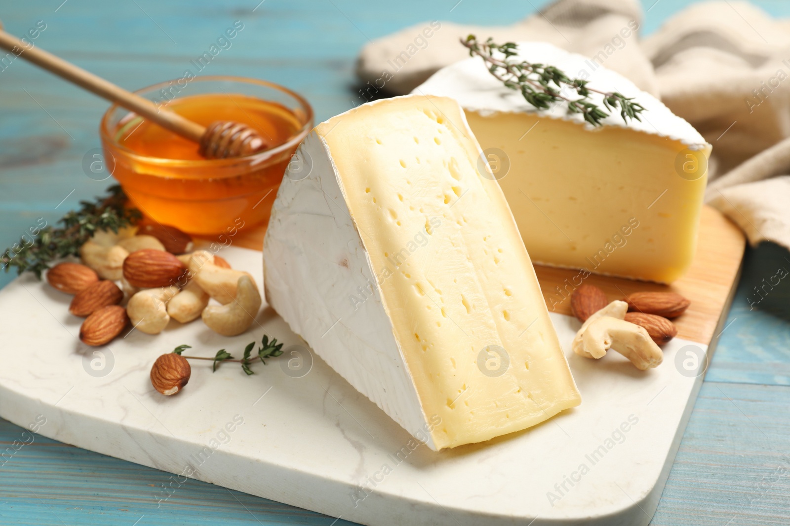 Photo of Tasty Camembert cheese with thyme, honey and nuts on light blue wooden table