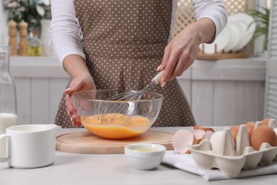 Photo of Woman whisking eggs in bowl at table indoors, closeup