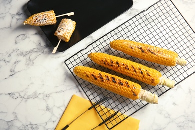 Cooling rack with grilled corn cobs on marble background, top view